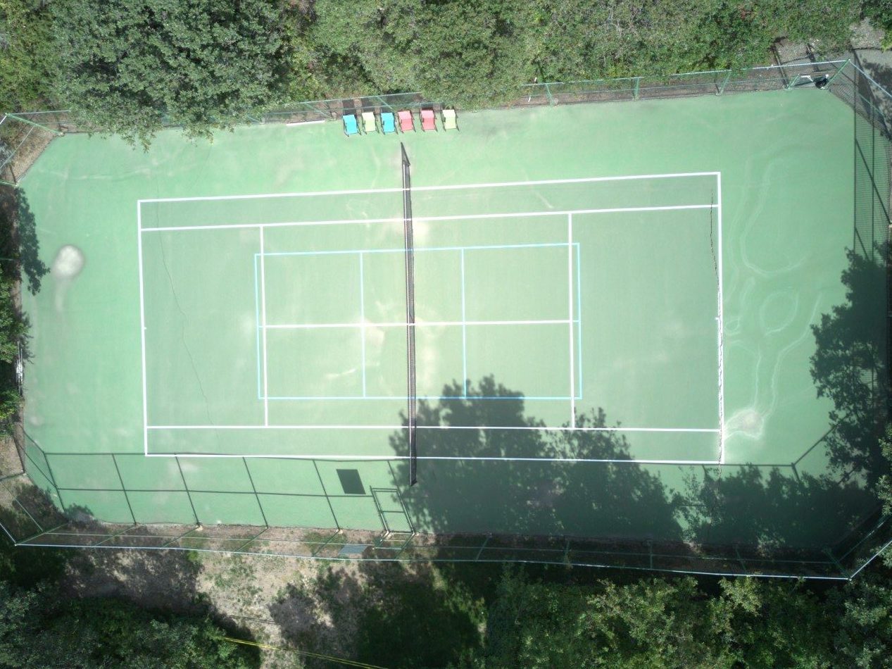 Worn, faded green tennis court before resurfacing, aerial view