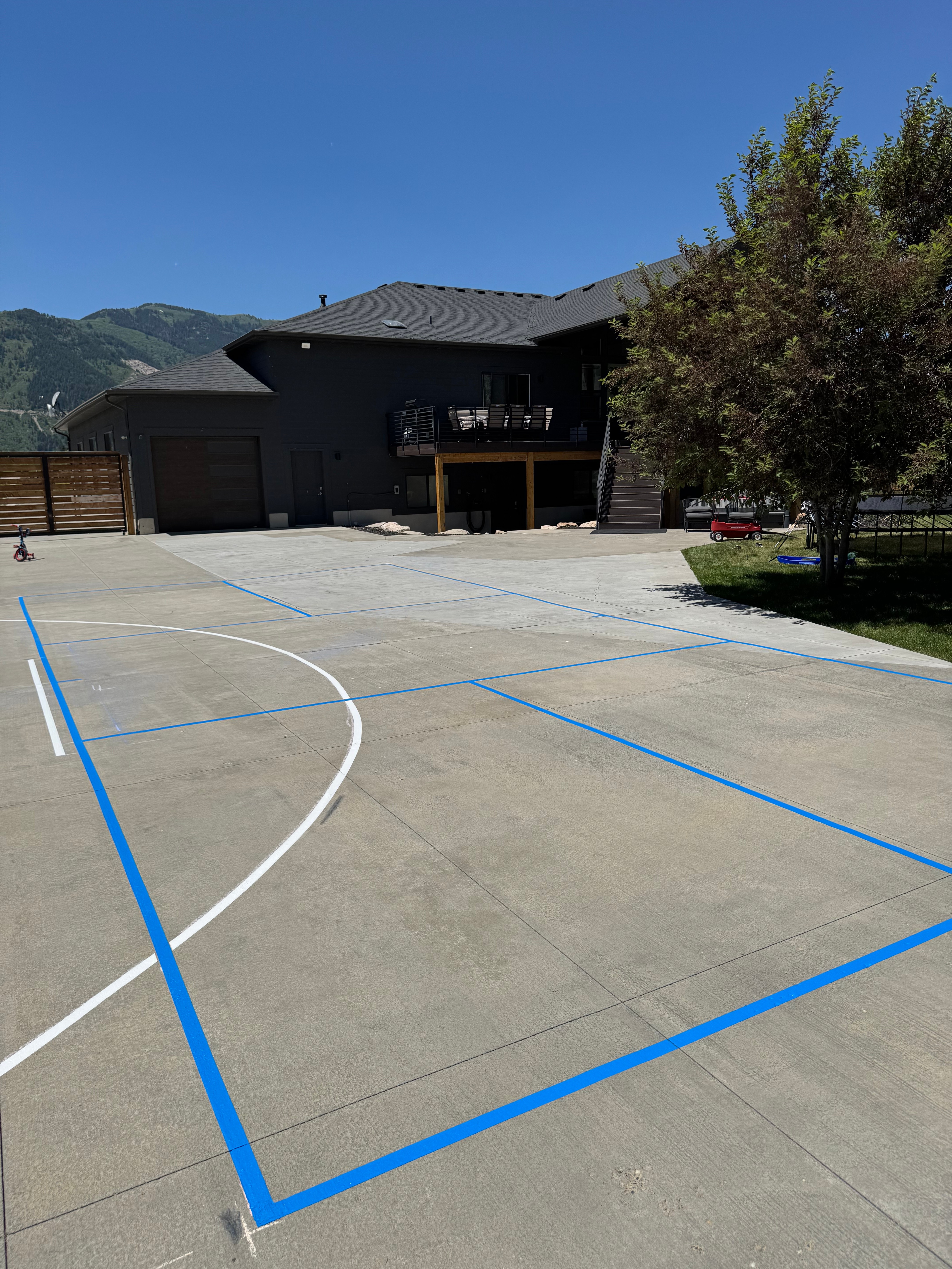Blue basketball key and three-point line striped on a concrete driveway court